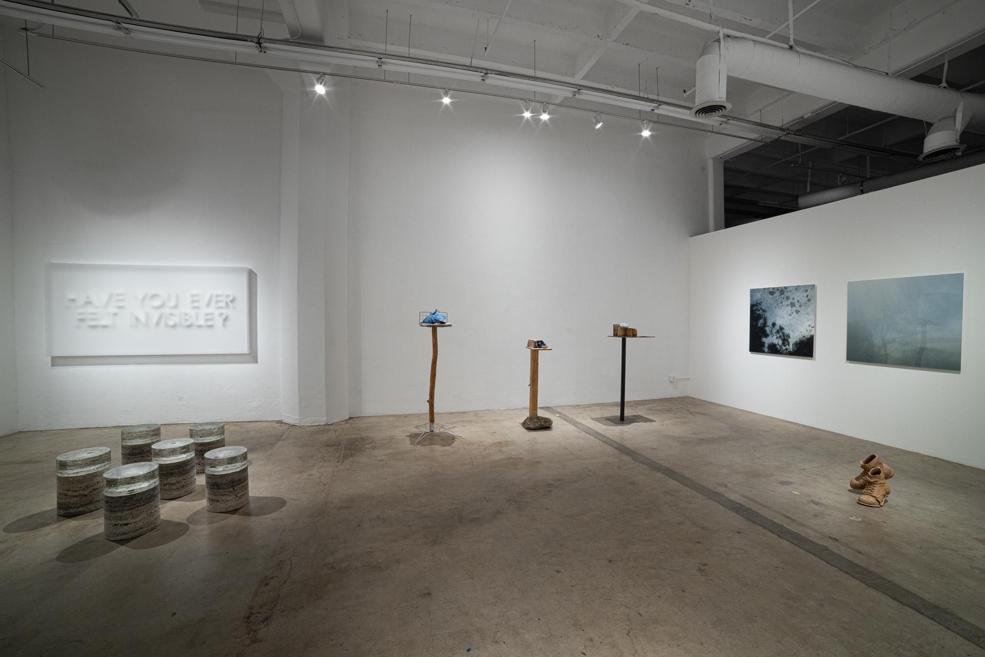 Stacked paper discs on the floor, a white relief text panel at left, wood stands with sculptures and two paintings on the far wall. Installation view, Valence: Azadeh Shladovsky & Daniel Wheeler, Track 16.