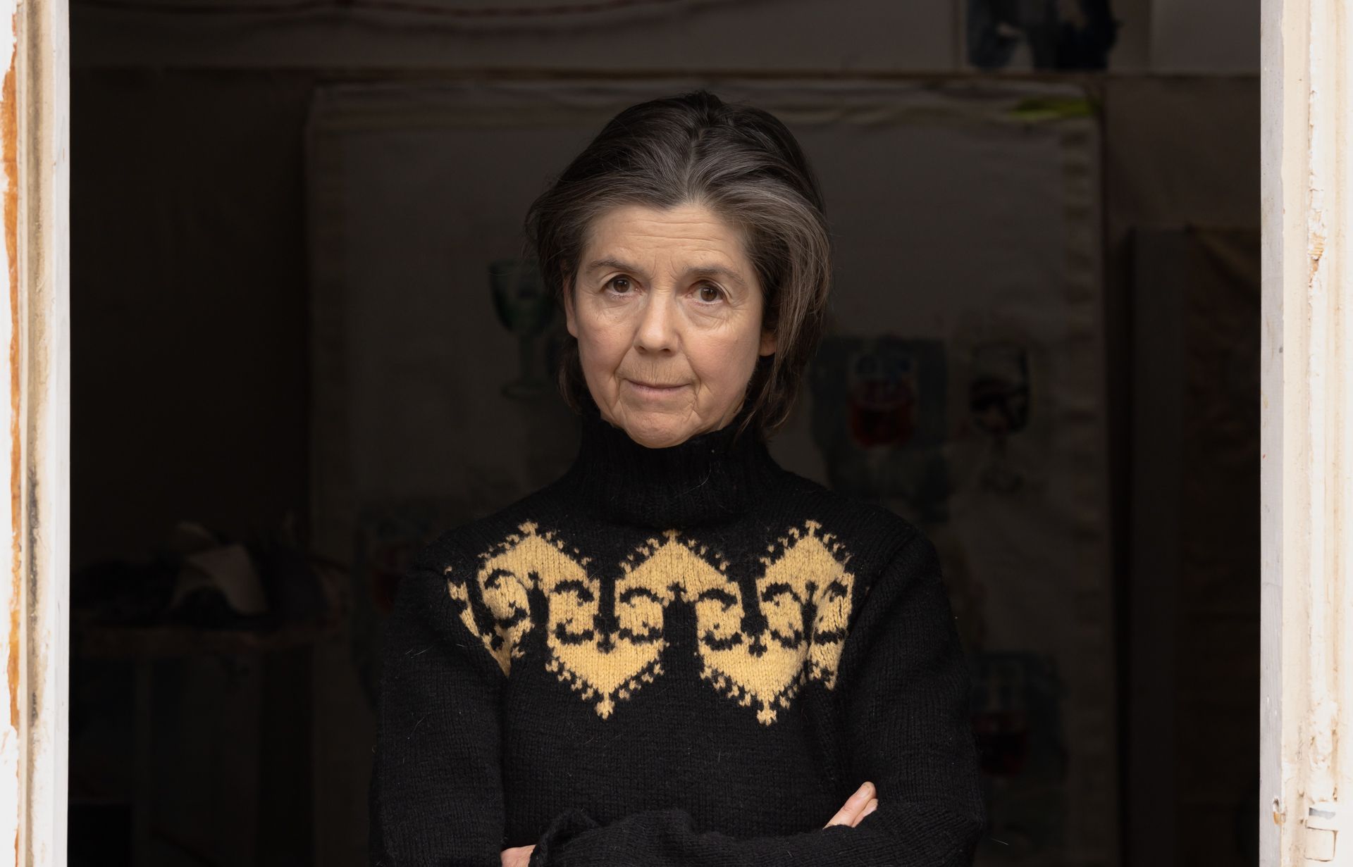 A woman in a black sweater is standing in a doorway with her arms crossed.