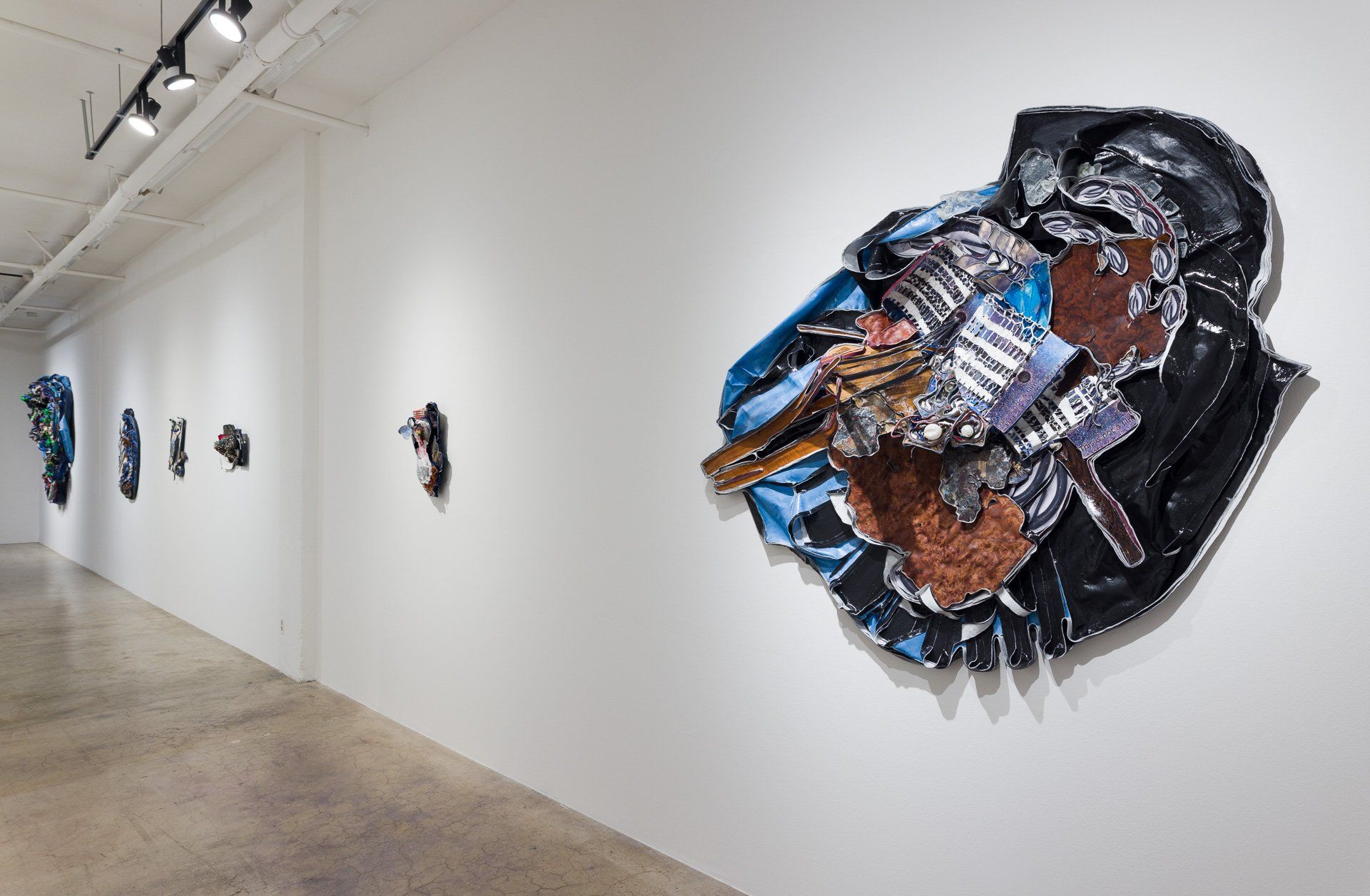 A row of paintings are hanging on a white wall in Track 16 Gallery.
