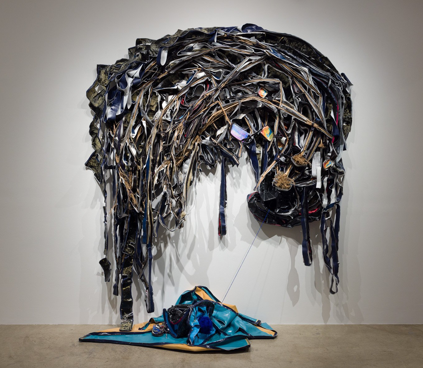 A large sculpture made of clothes is hanging on a wall.