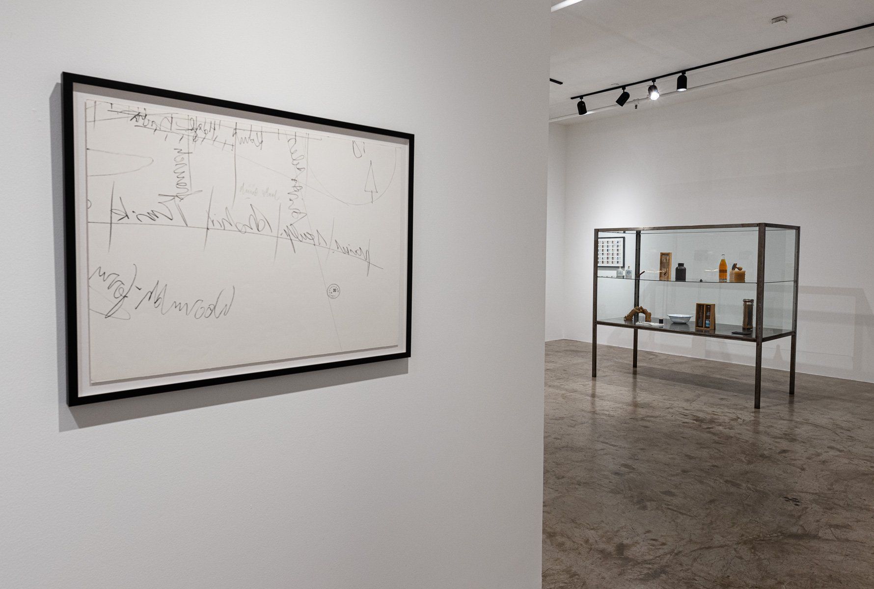 A framed picture is hanging on a white wall next to a glass display case.