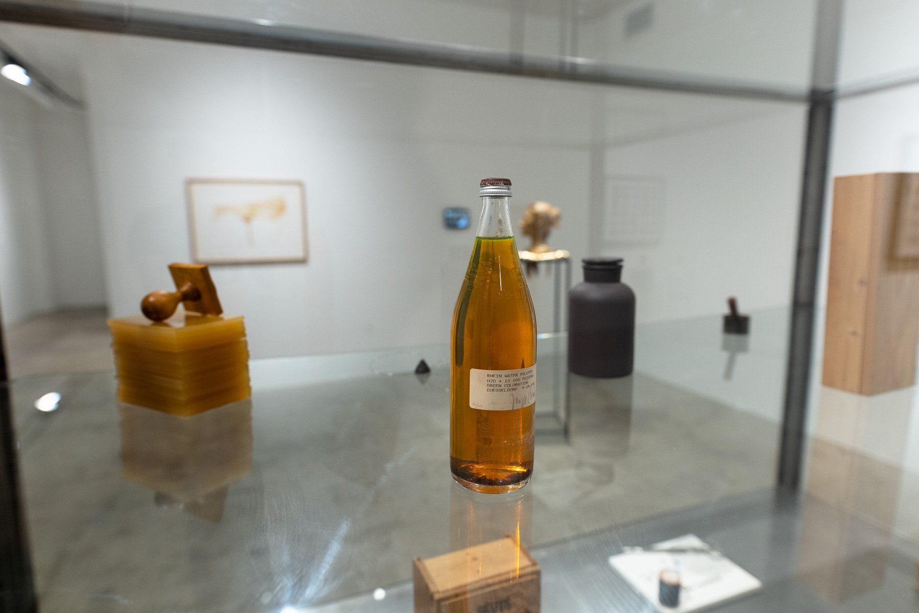 A bottle of liquid is sitting on a glass table in a glass case.
