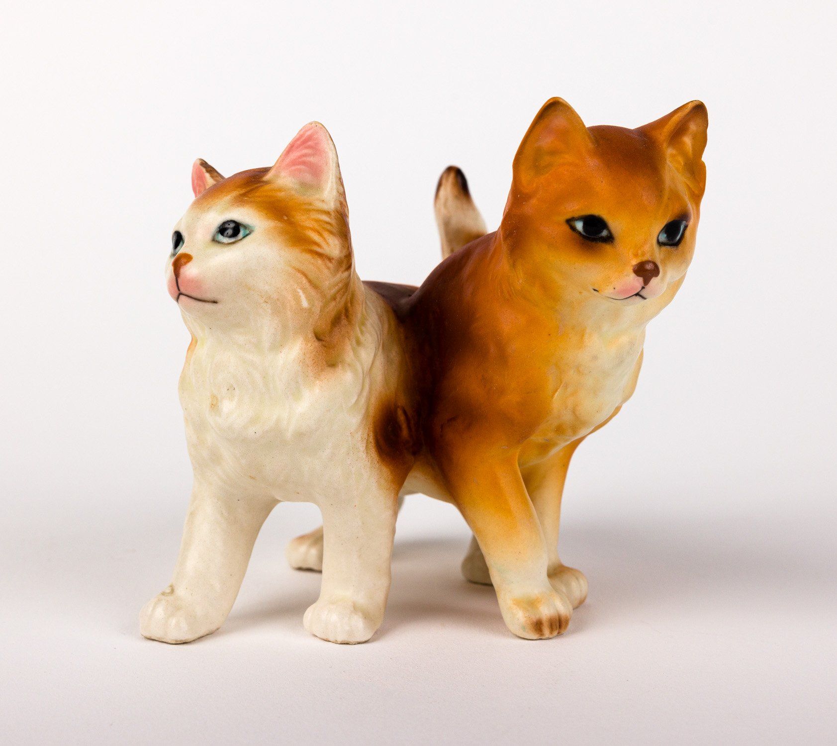 Two figurines of cats standing next to each other on a white background