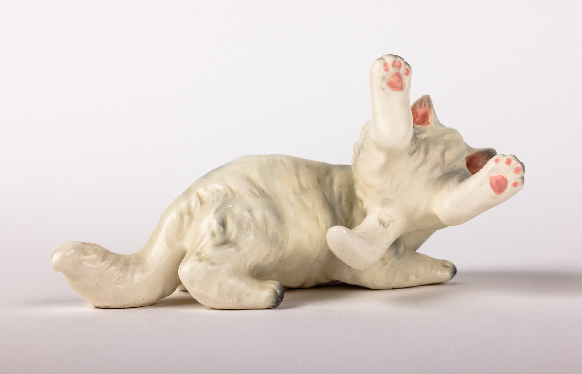 A statue of a white cat laying on its back with its paws up.