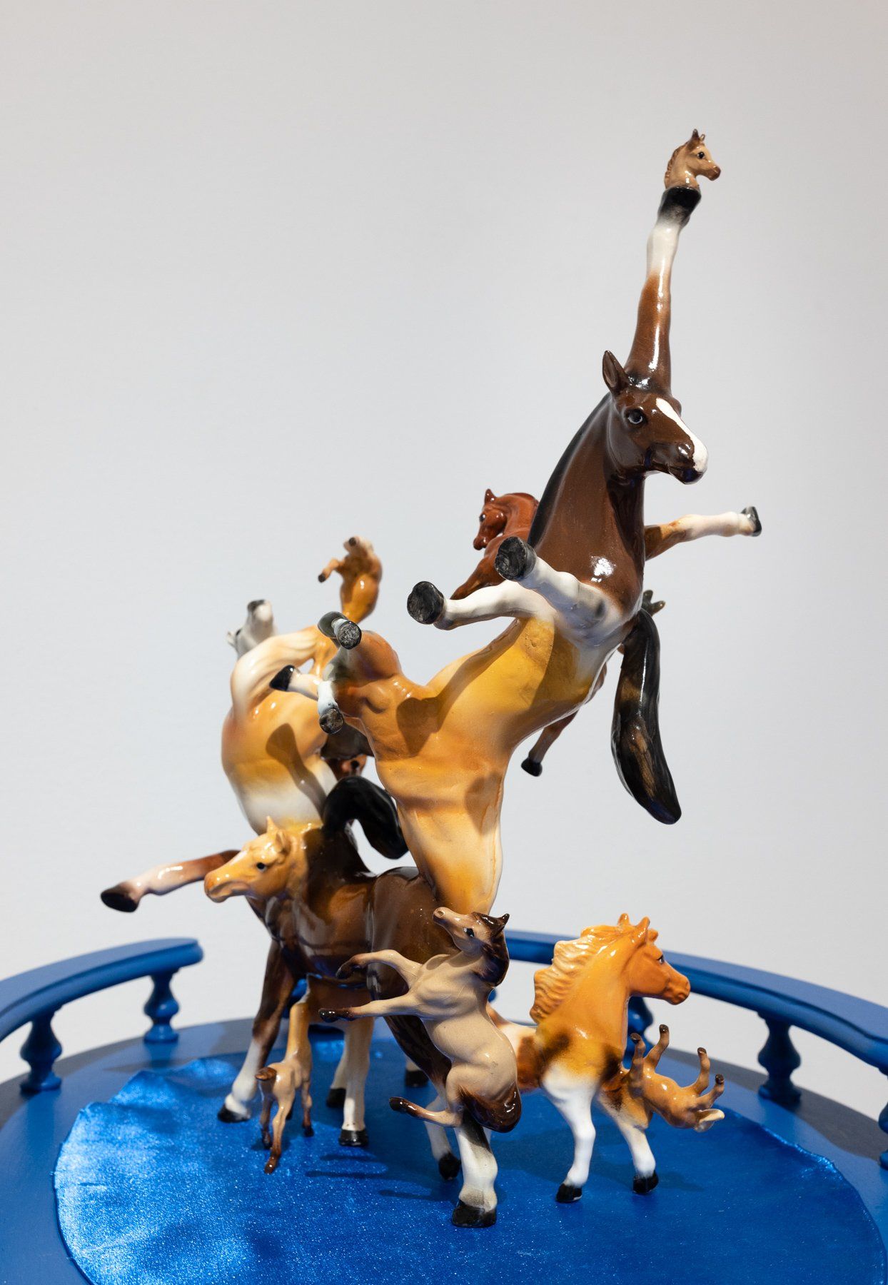 A group of toy horses are standing on top of each other on a blue surface.