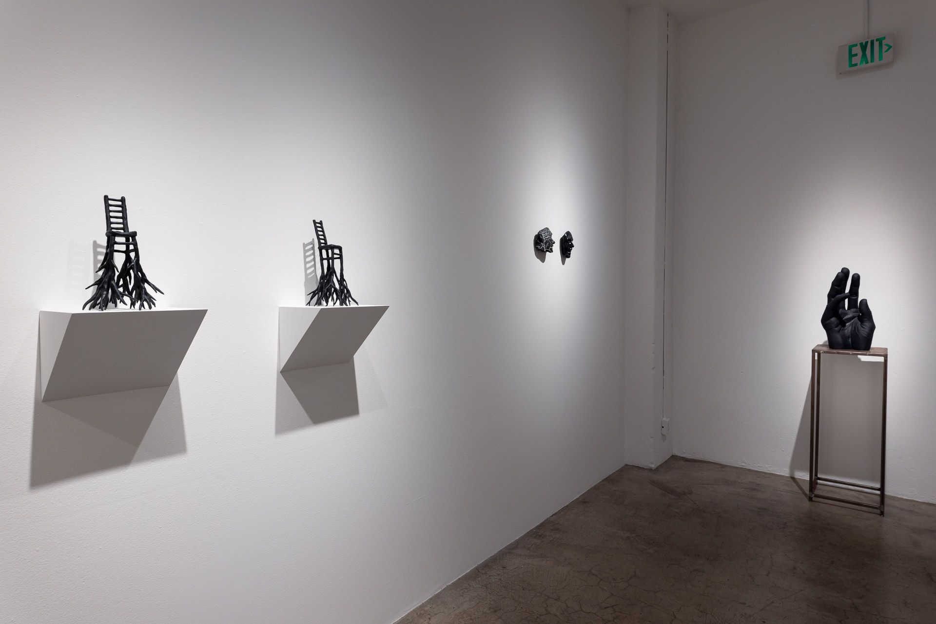 Minimalist art gallery wall with small sculptures on white shelves and a pedestal display in the corner.