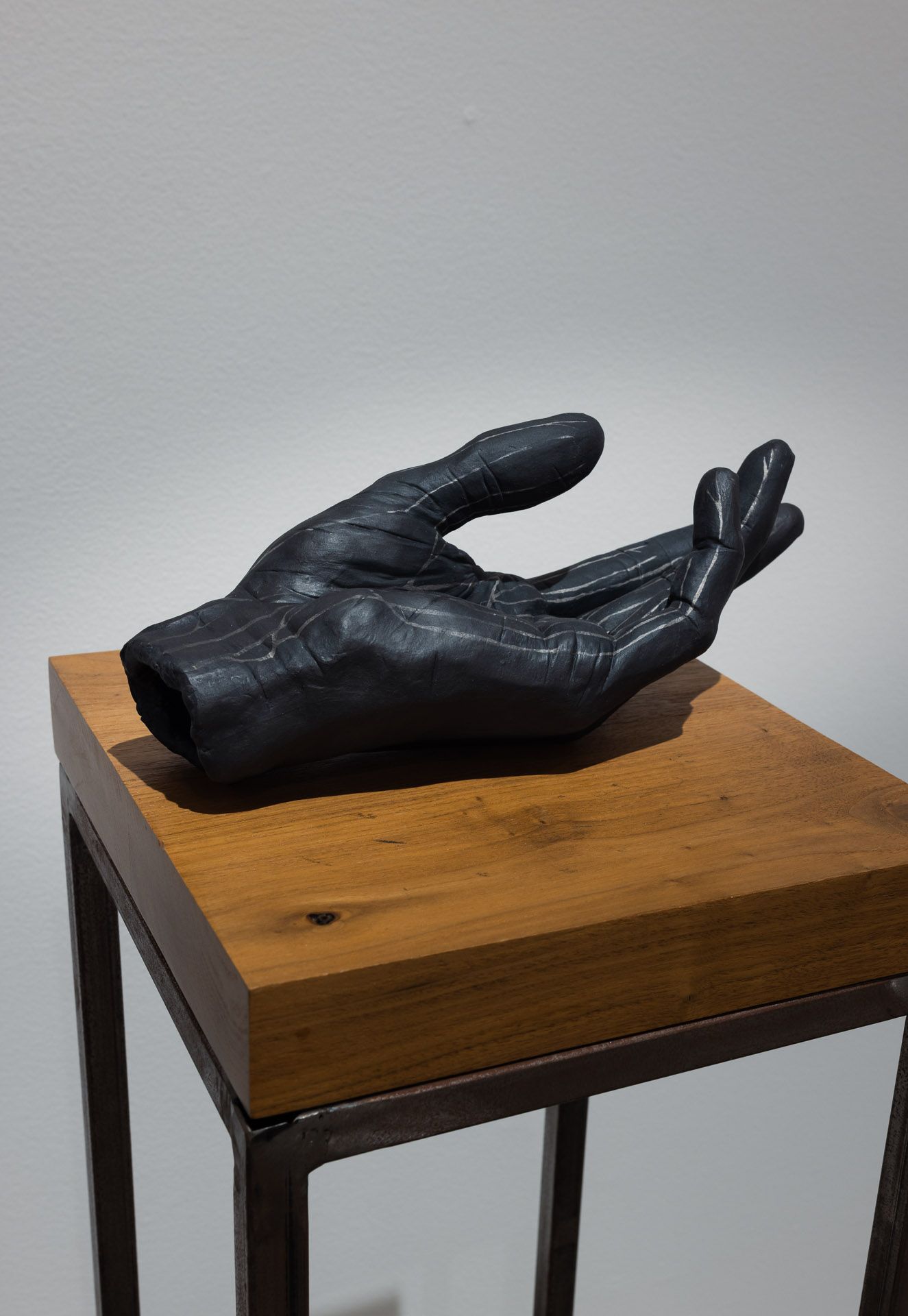 Black sculpted hand resting on a wooden pedestal against a plain wall.
