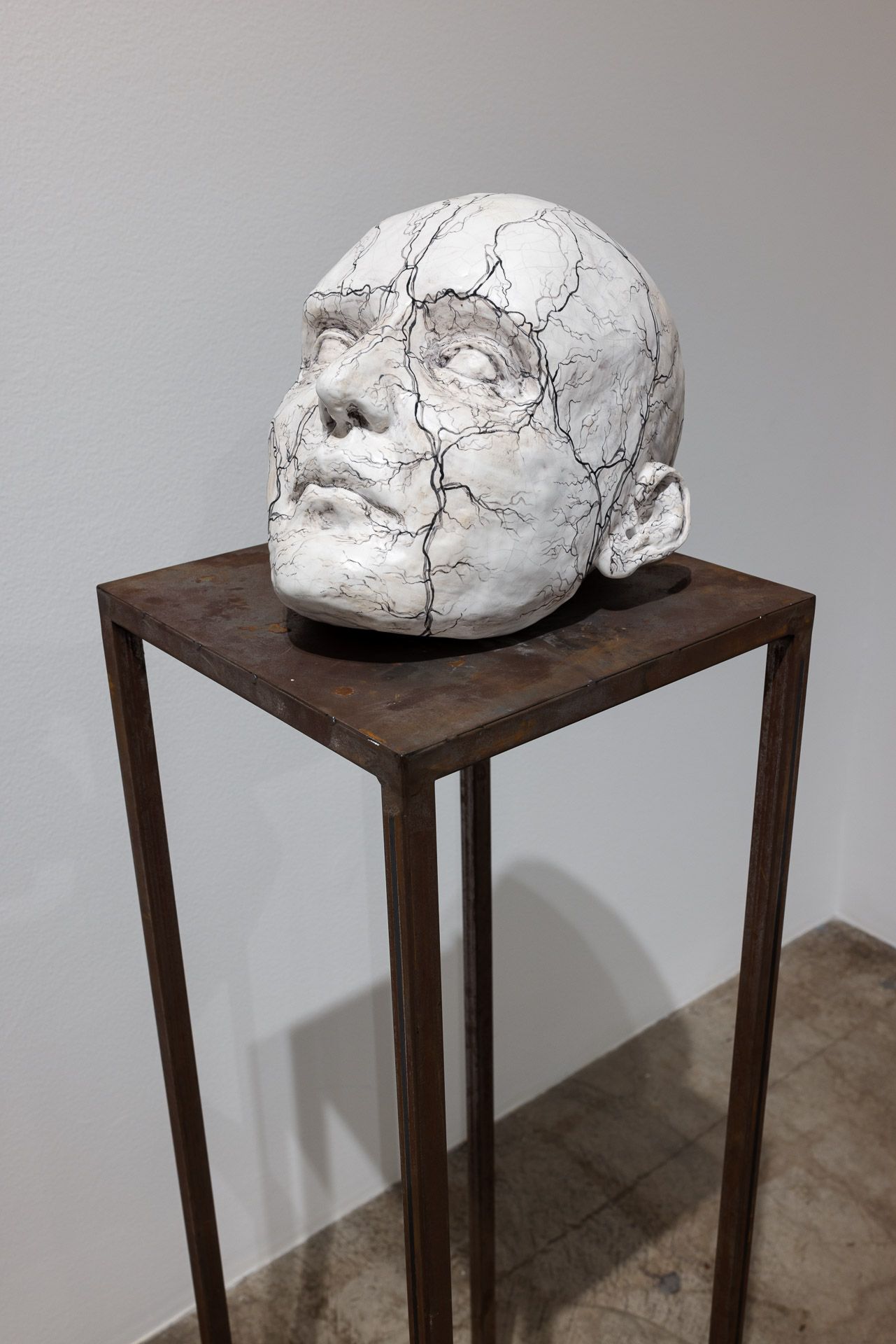White sculpted face bust on a dark wooden pedestal table in a plain gallery-like room.