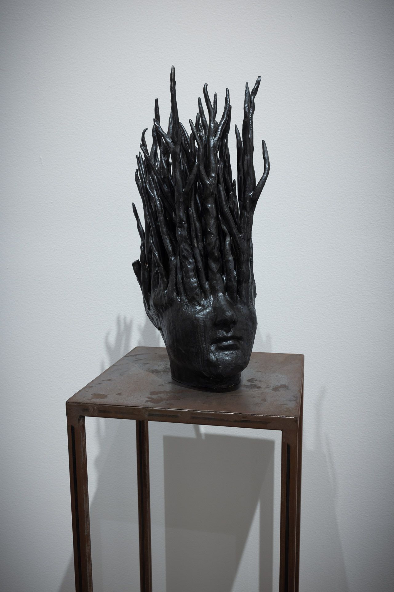 Black sculptural head with tall spiky branches on a small wooden table against a white wall