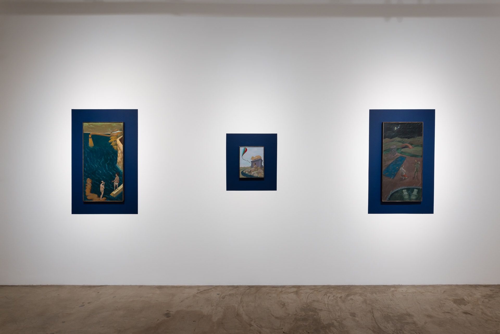 Three paintings are hanging on a white wall in a room.
