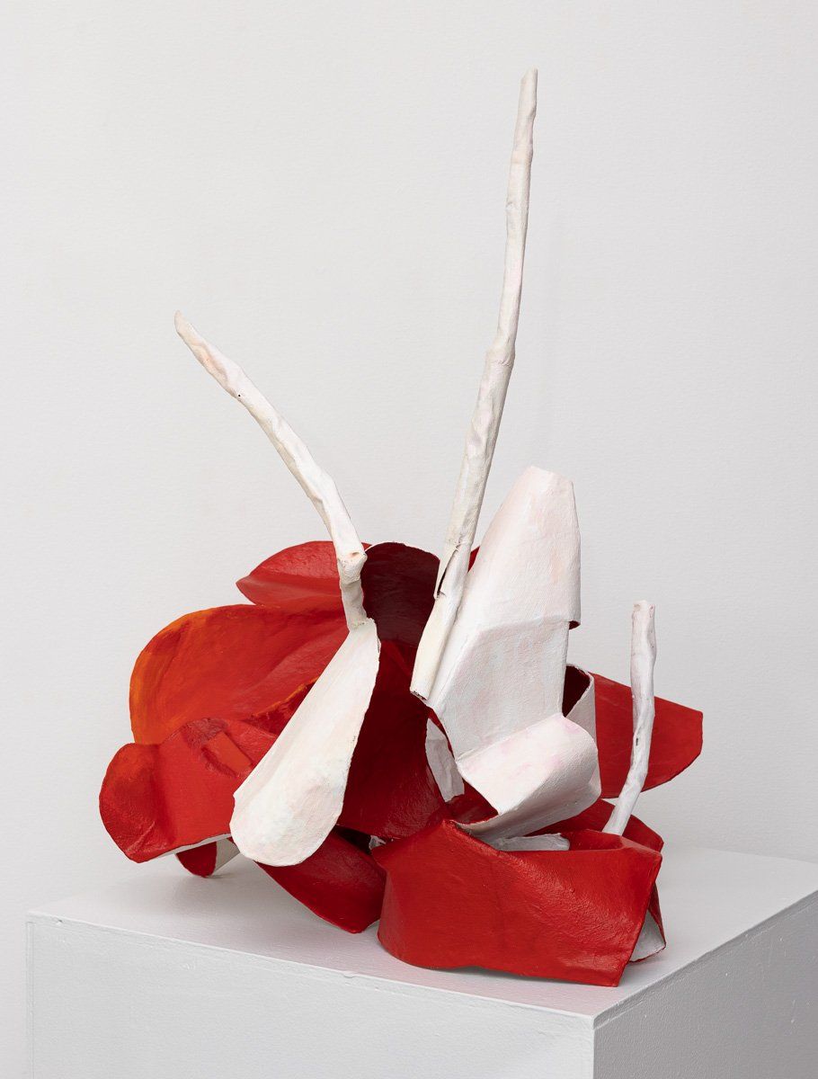 A red and white sculpture is sitting on a white cube