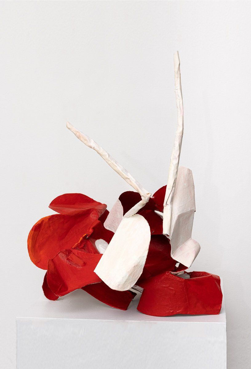 A red and white sculpture is sitting on a white cube