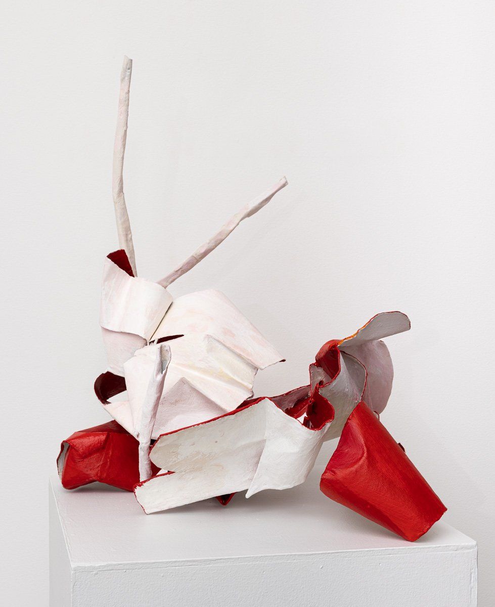 A white and red sculpture is sitting on a white cube