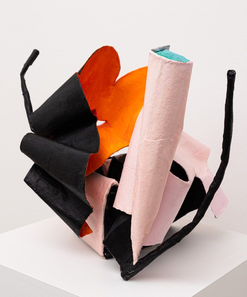 A black and orange sculpture is sitting on a white cube