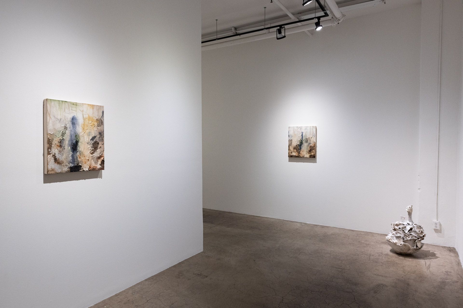 A room with two paintings on the wall and a sculpture on the floor.