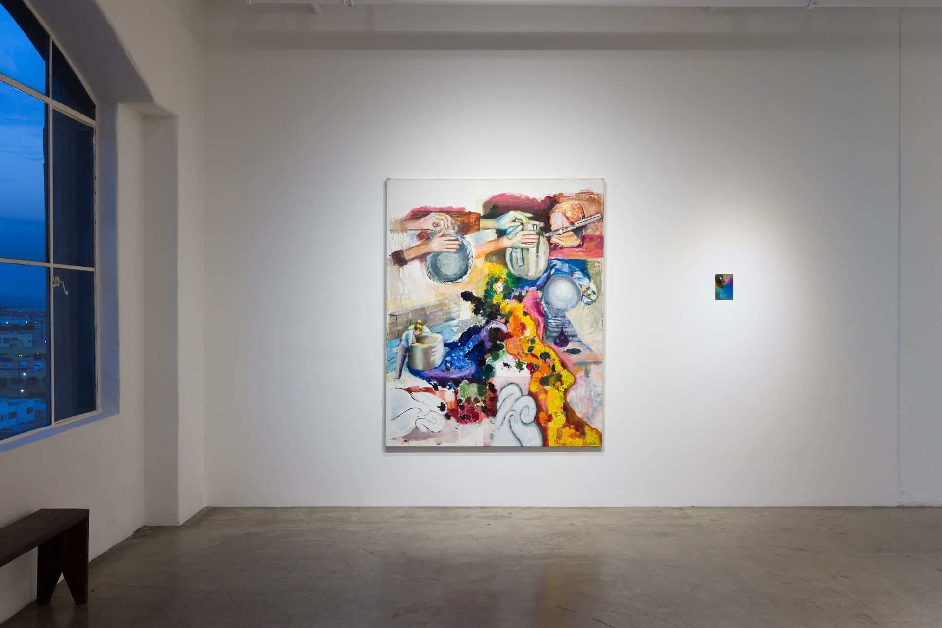 Large colorful painting of tangled forms and a tiny blue painting on a white wall, with a tall window and bench at left. Installation view, Margarete Hahner: Heimlich, Track 16.