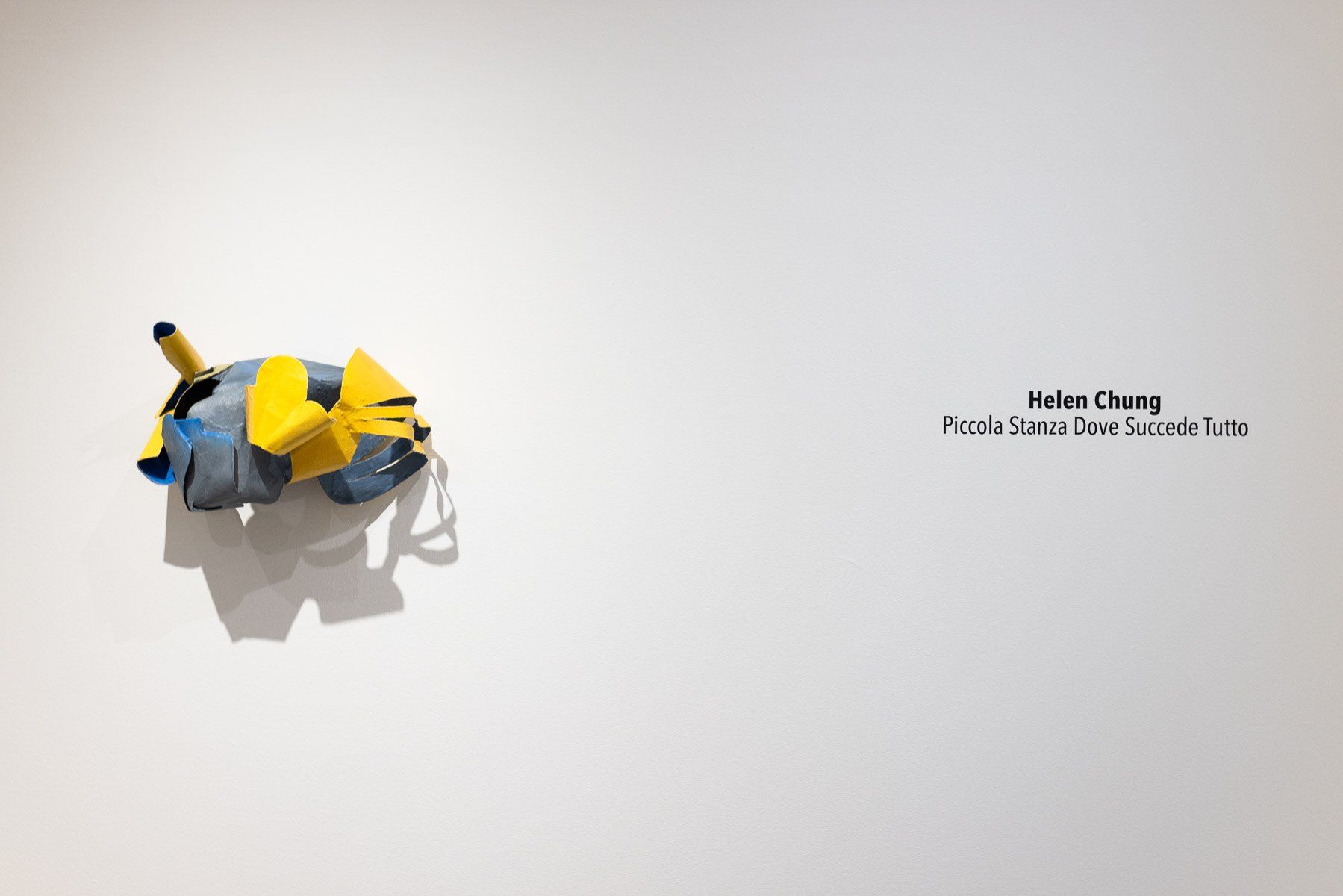 A yellow and blue sculpture is hanging on a white wall.