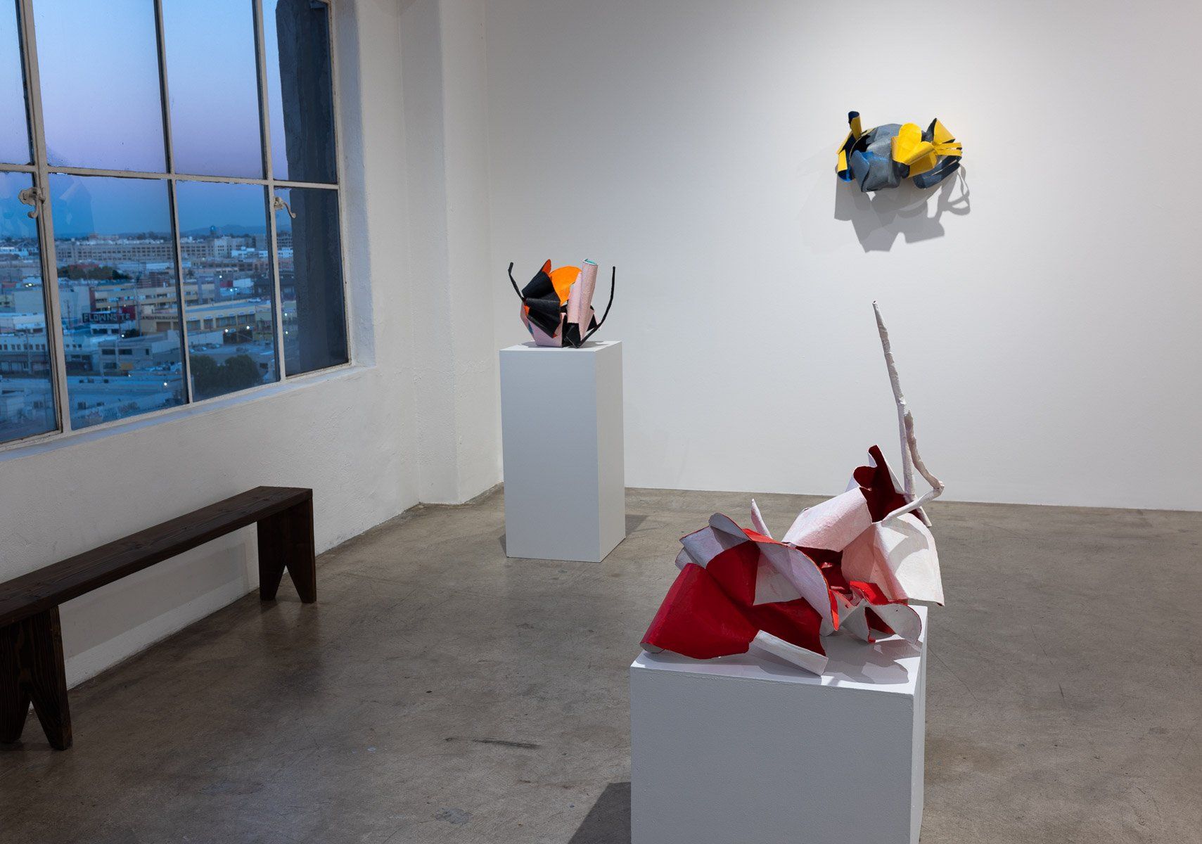 A room with a bench and three sculptures on display.