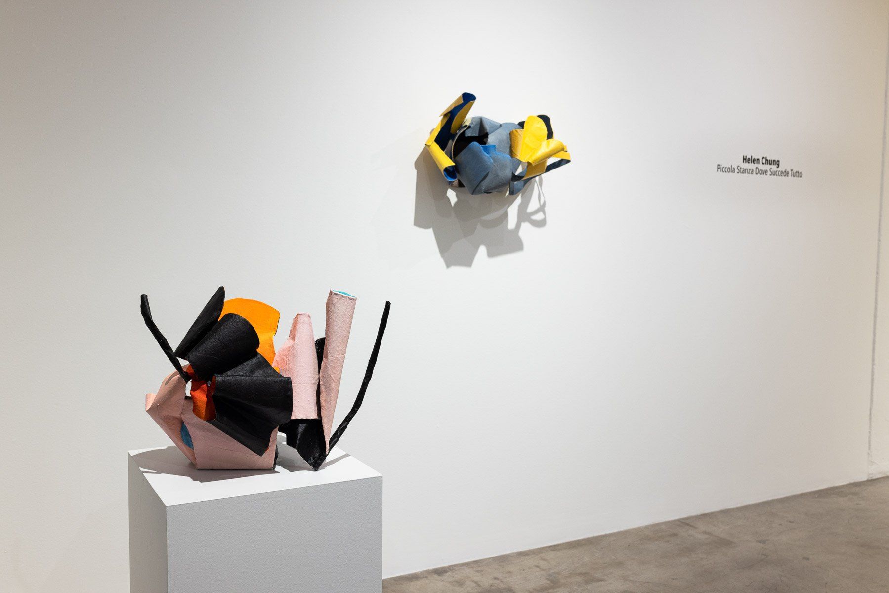 Two sculptures are on display in a room with a white wall.