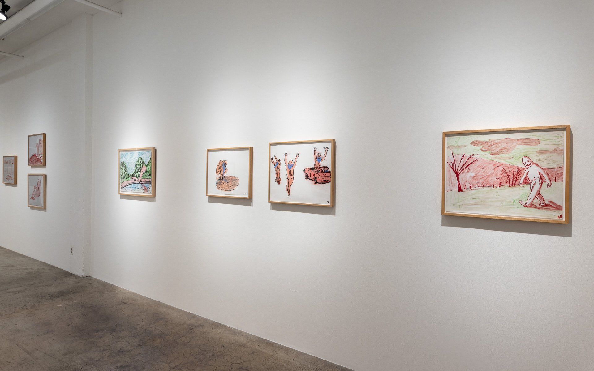 A row of paintings are hanging on a white wall in a museum.