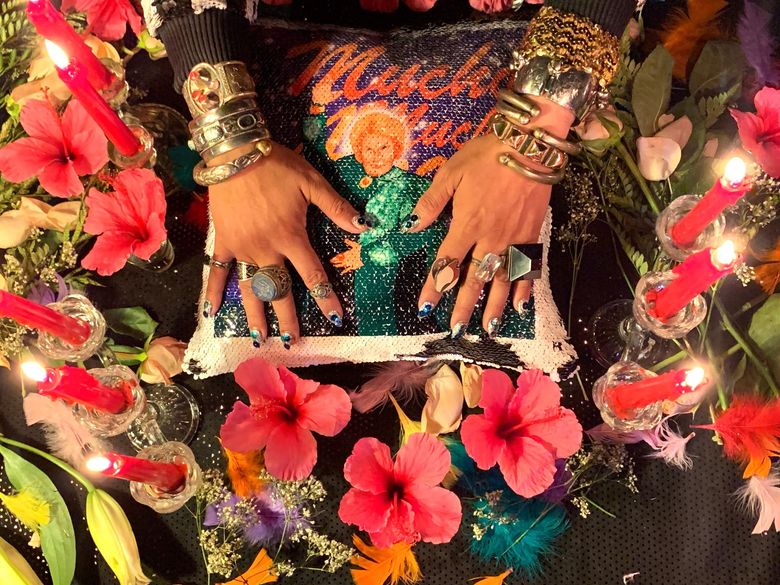 Jeweled hands on top of a pillow surrounded by a ring of flowers and candles.