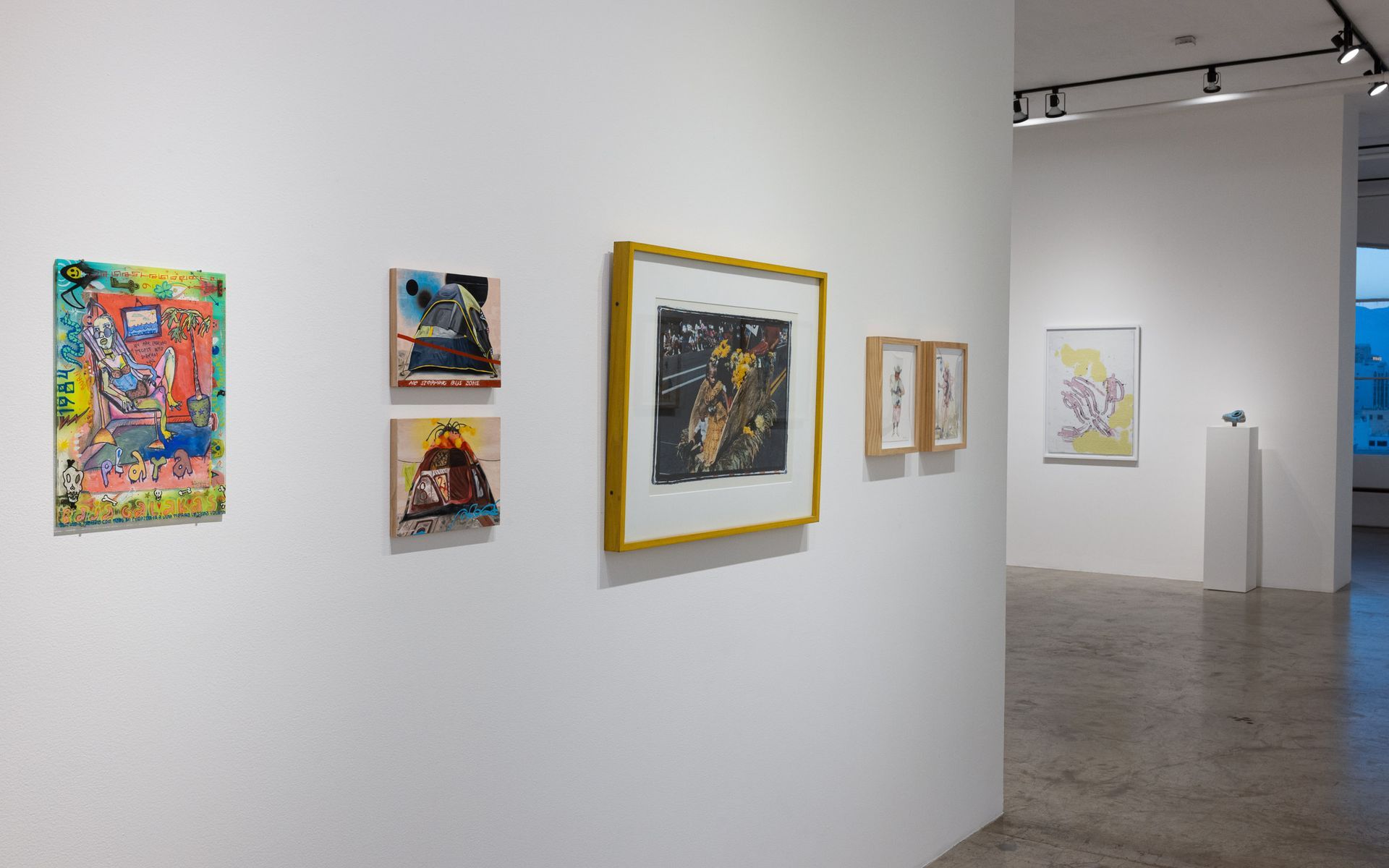 Art gallery wall with colorful framed paintings and prints in a bright exhibition space. Summer Bullet Sings, an exhibition of thirty-five artists organized by gallery director Sean Meredith and curator Diana Sardaryan.