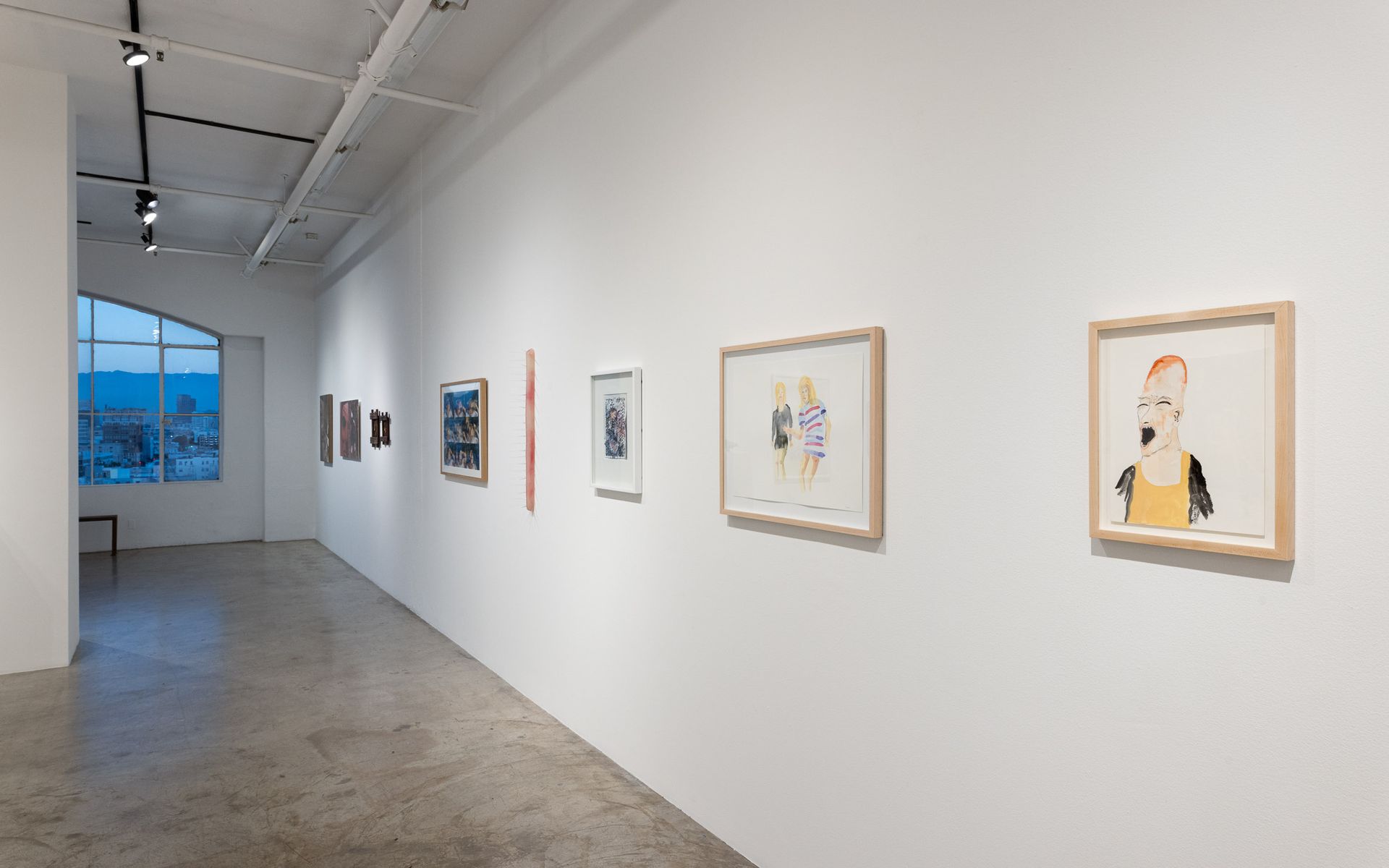 Minimalist gallery hallway with framed artworks on white walls and a large window at the end. Summer Bullet Sings, an exhibition of thirty-five artists organized by gallery director Sean Meredith and curator Diana Sardaryan.