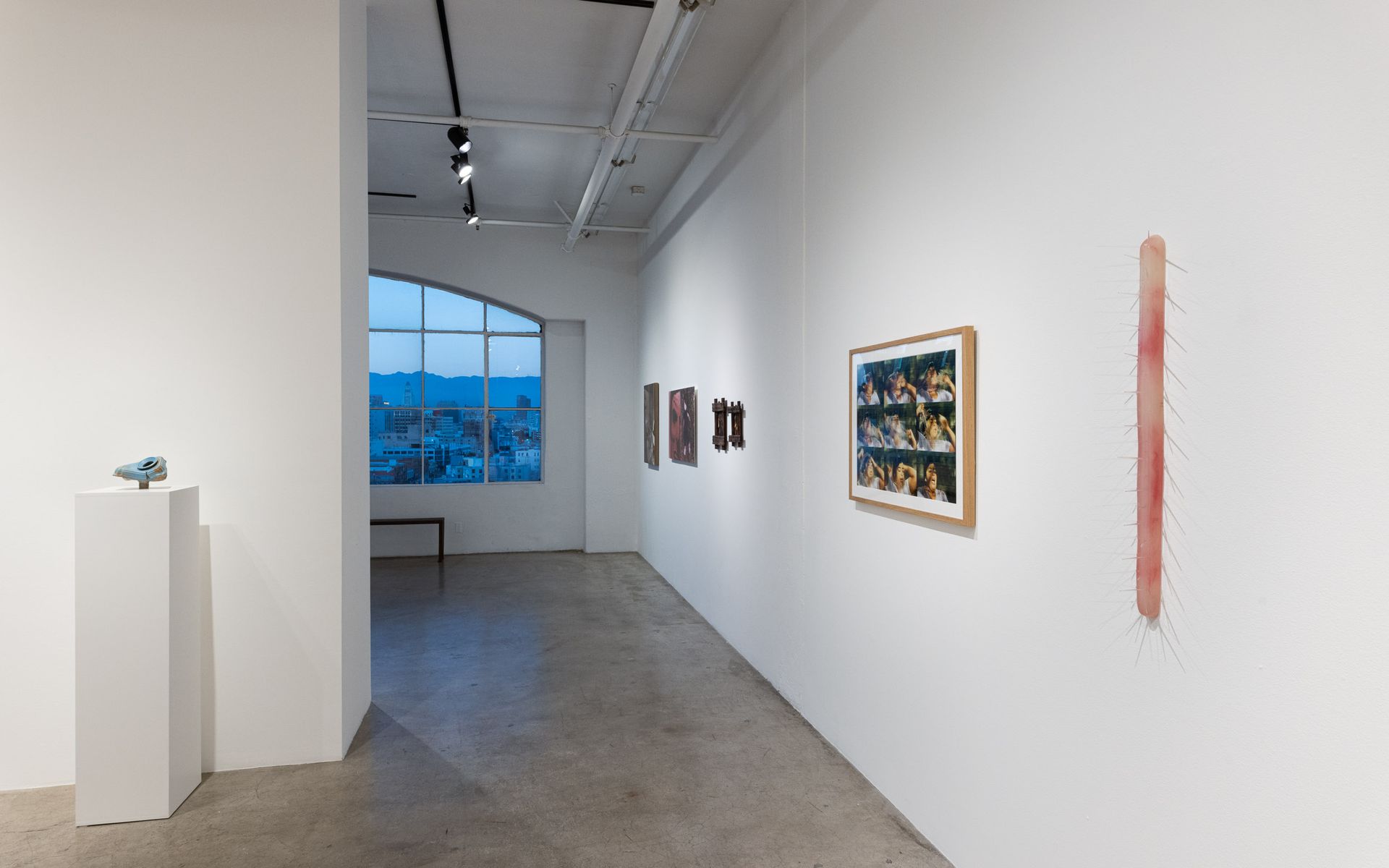 Modern art gallery hallway with white walls, framed artworks, and a large window at the end. Summer Bullet Sings, an exhibition of thirty-five artists organized by gallery director Sean Meredith and curator Diana Sardaryan.