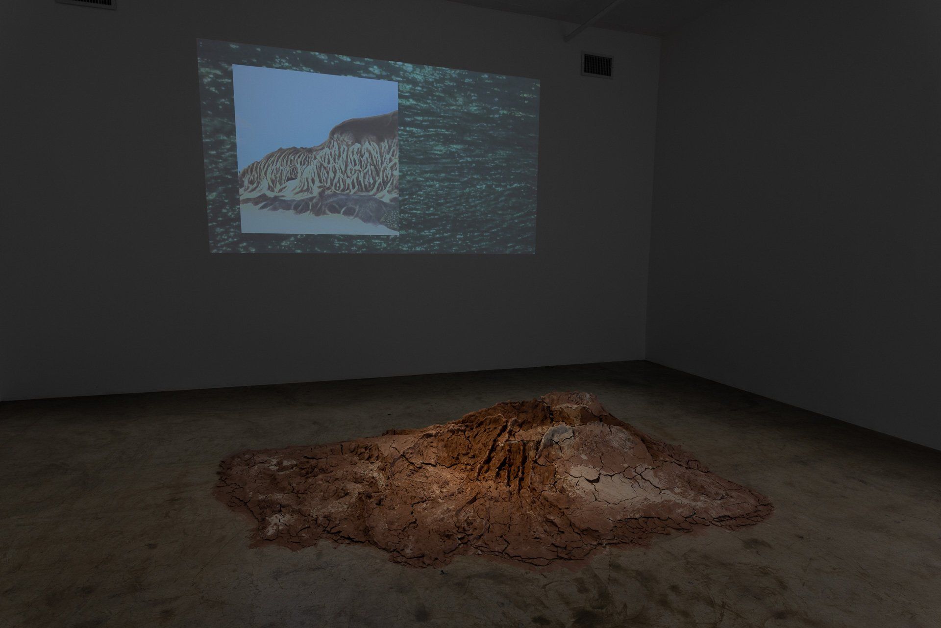 A room with a large pile of dirt on the floor and a projection screen on the wall.