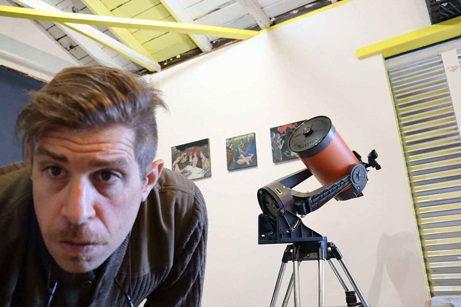 A man stands in front of a telescope in a room