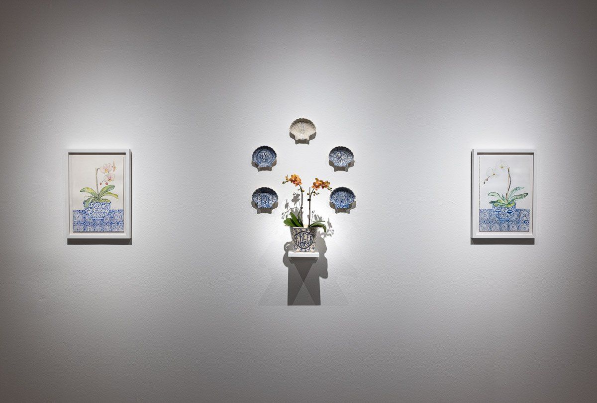 A vase of flowers is sitting on a table in front of three paintings on a wall.