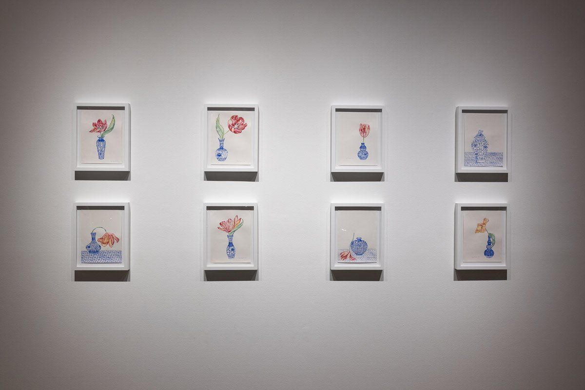 A row of paintings of flowers in vases on a wall.