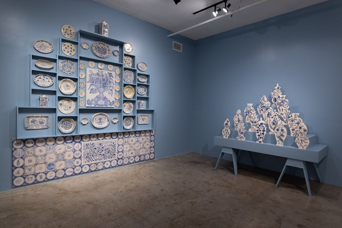 A room with blue walls and a shelf filled with plates and vases.