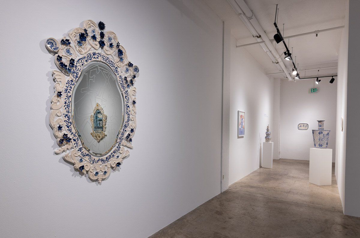 A large mirror is hanging on a white wall in a museum.
