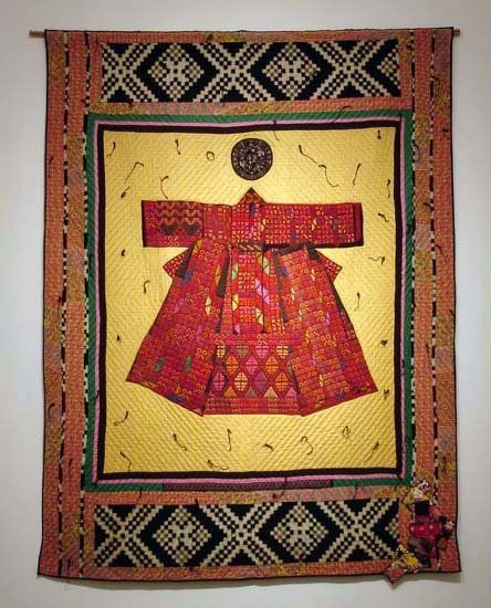 A quilt with a red dress on it is hanging on a wall