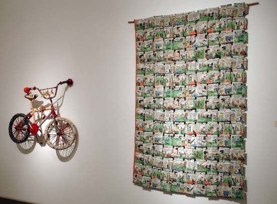 A bicycle is hanging on a wall next to a quilt