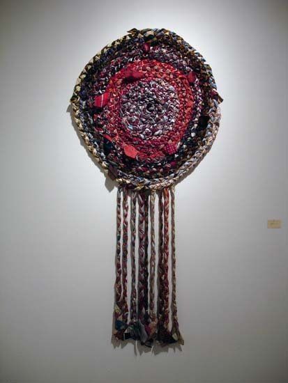 A red and purple circle with fringe is hanging on a white wall