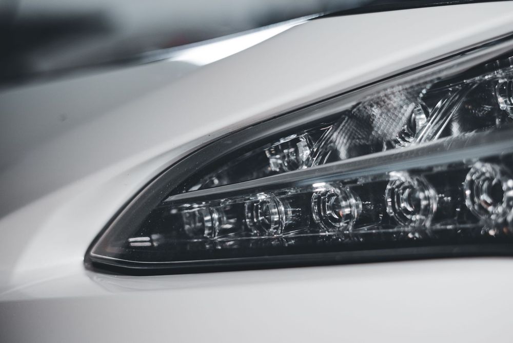Close-up of a white car’s front headlight and hood