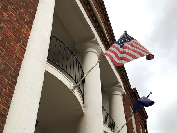 American flag and blue flag on building with white columns and red brick facade.
