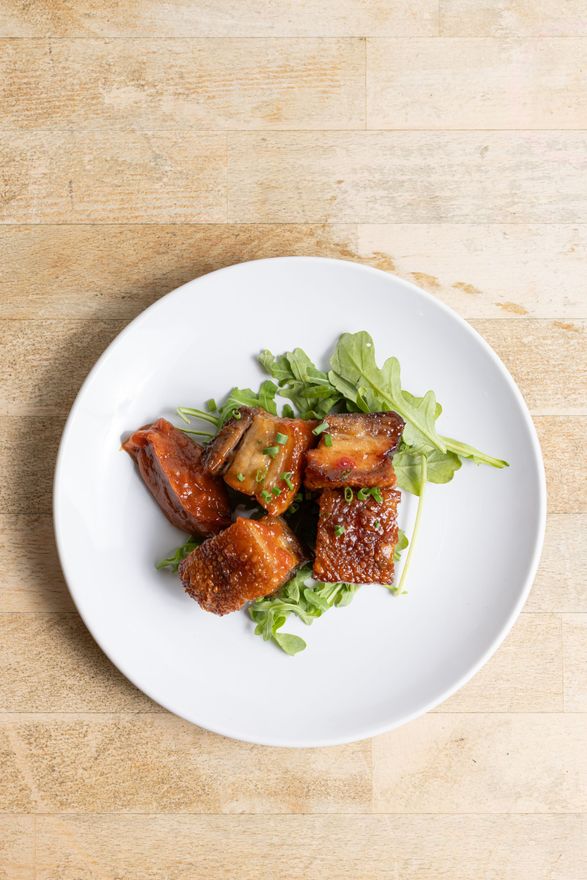 A white plate topped with meat and greens on a wooden table.