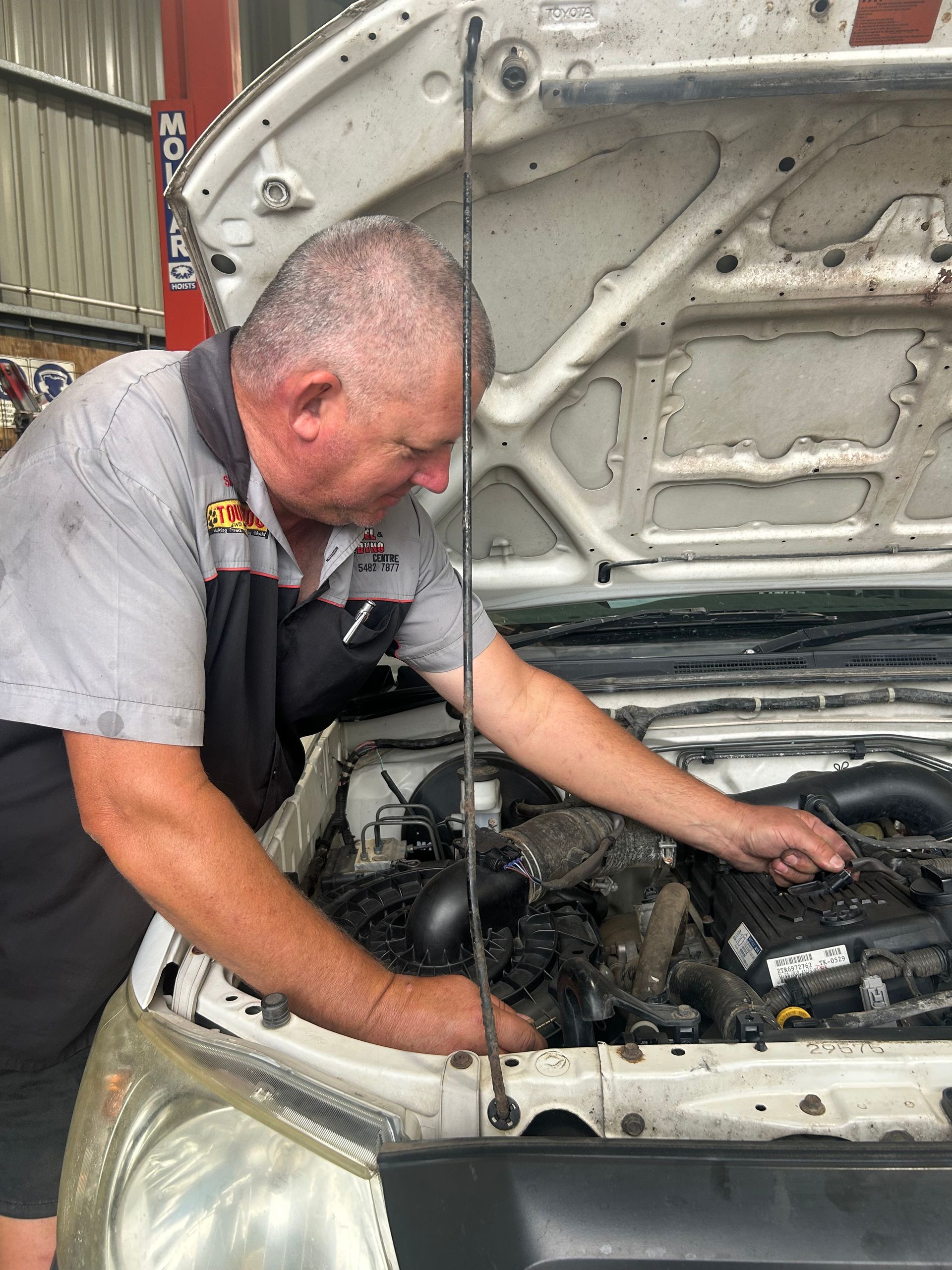 Mechanic inspecting an engine under the open hood of a white car in a garage. — Gympie Diesel & Dyno Centre in Glanmire, QLD