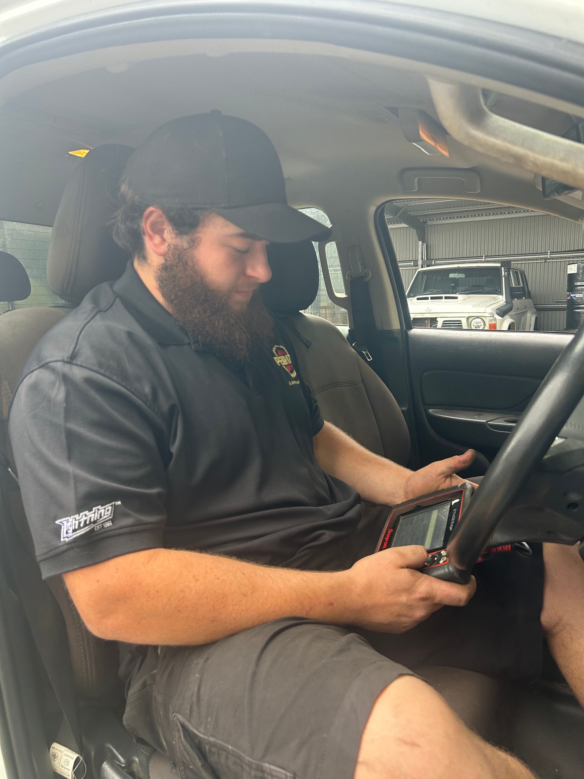 Mechanic in a car using a diagnostic tool. Wearing a black cap and shirt, looking at the device. — Gympie Diesel & Dyno Centre in Glanmire, QLD