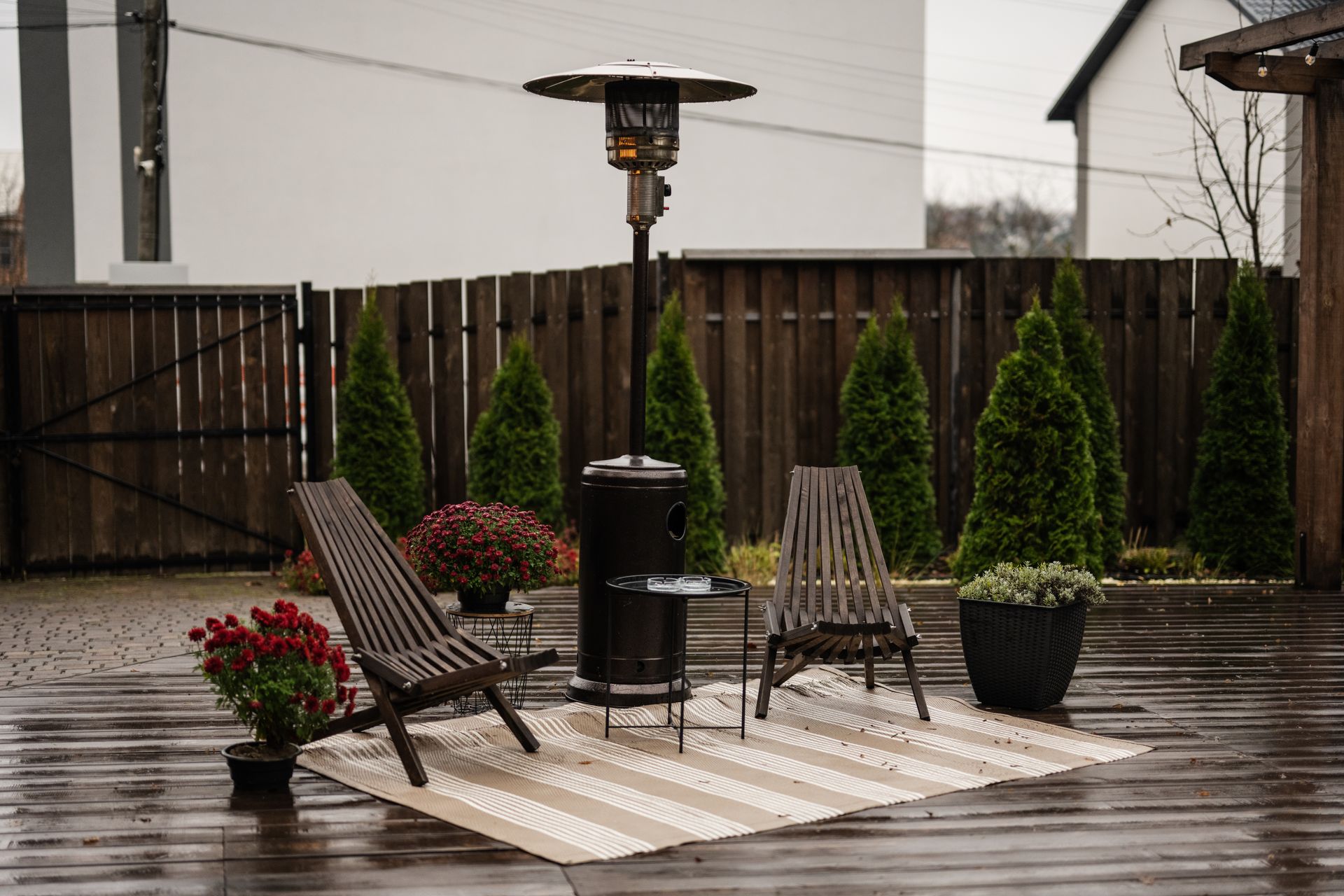 A wooden deck with chairs , a heater , and a rug.