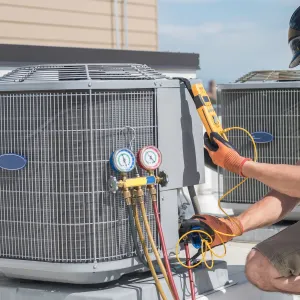 Happy Heating and Cooling LLC - A man is working on an air conditioner on the roof of a building.