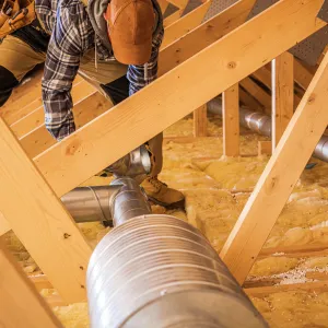 Happy Heating and Cooling LLC - A man is working on a pipe in the attic of a house.