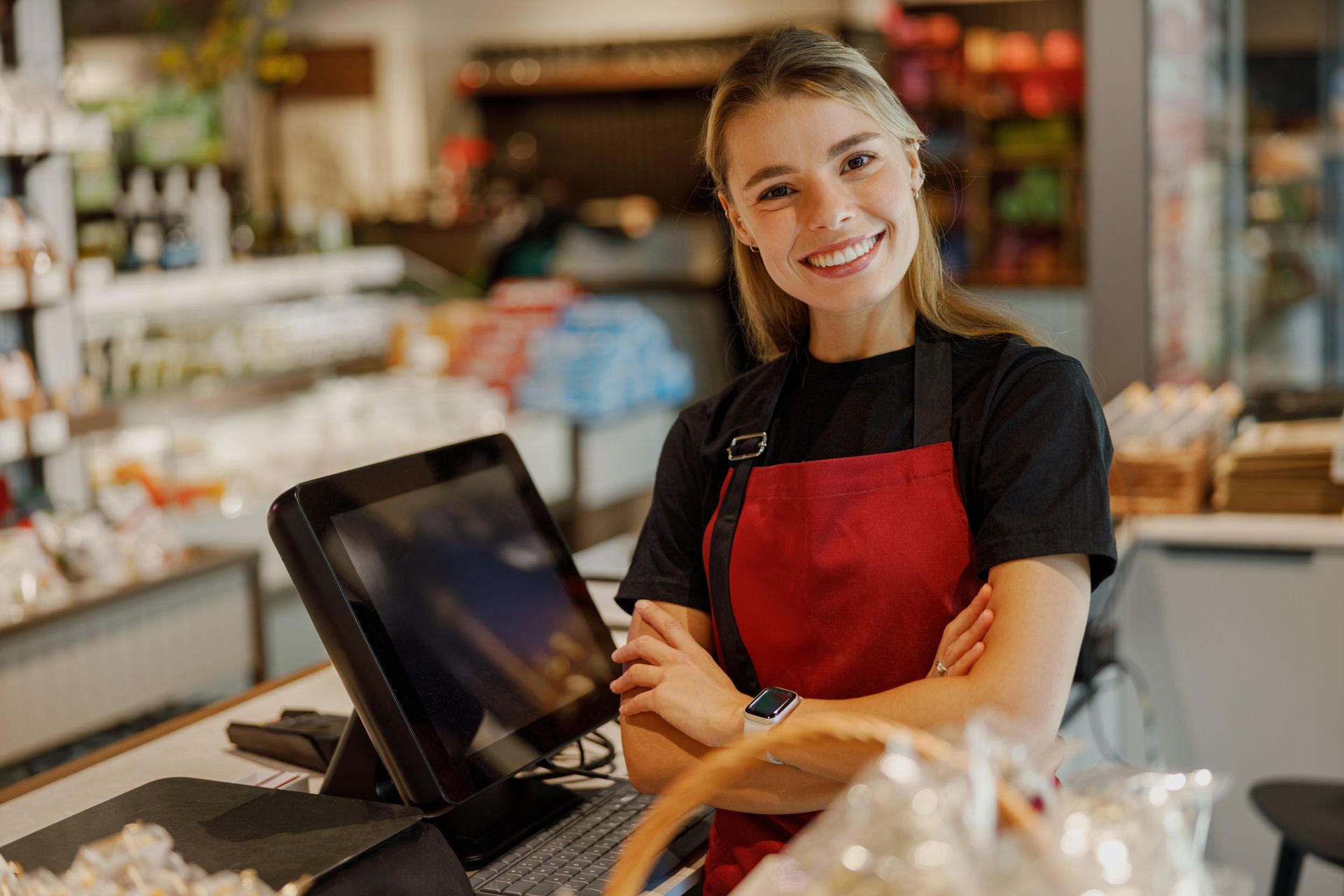 Woman in red apron smiles behind a checkout counter in a store