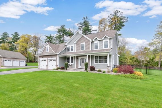 Gray two-story suburban house with white trim, large green lawn, and attached garage under a partly cloudy sky