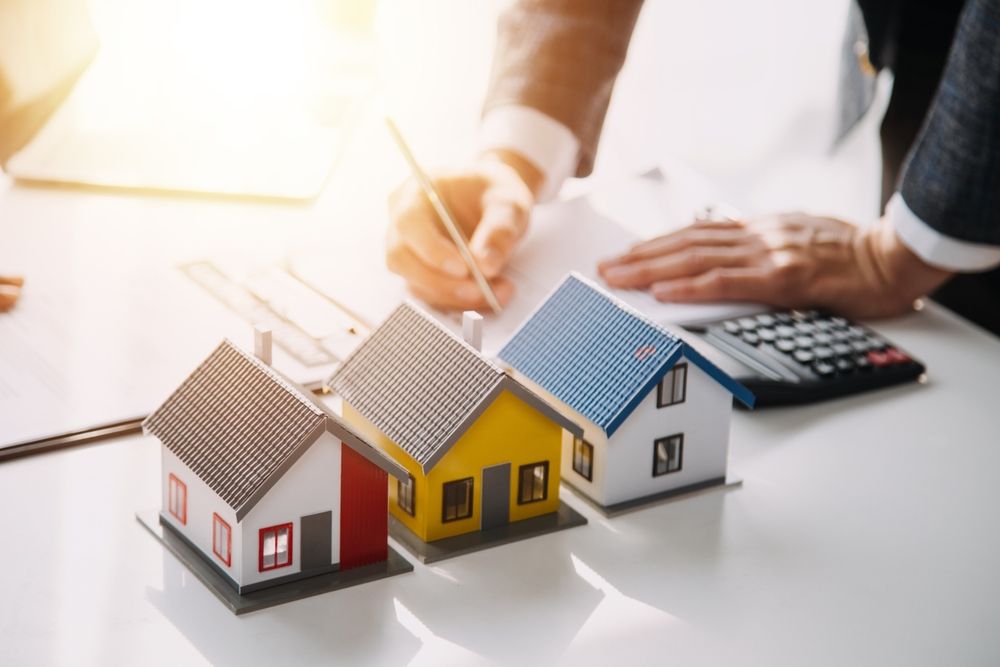 Miniature houses on a desk with hands, calculator, and financial documents in the background