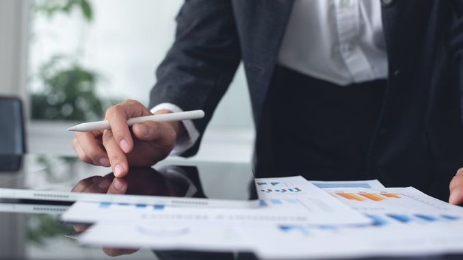 Businessperson pointing at financial charts and papers on a desk in an office