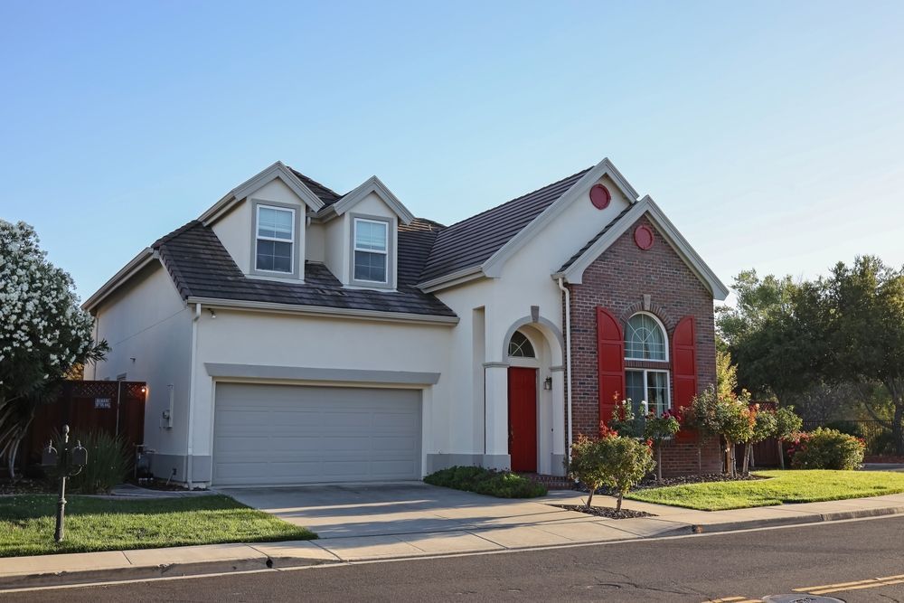 Suburban house with white garage, red front door, and brick accents on a sunny street